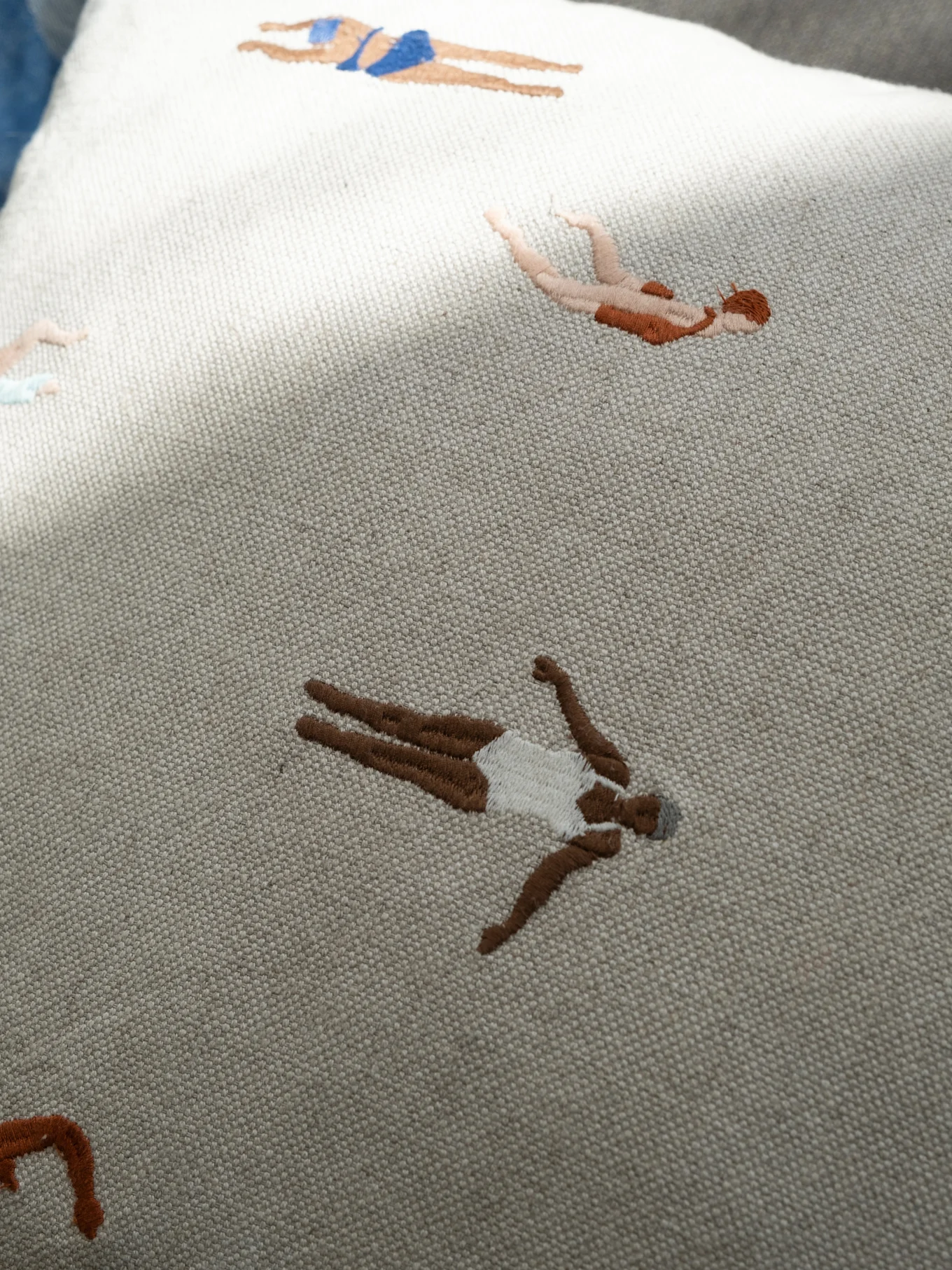 Tissu brodé de couleur claire avec des nageurs stylisés de différentes carnations et en maillot de bain.