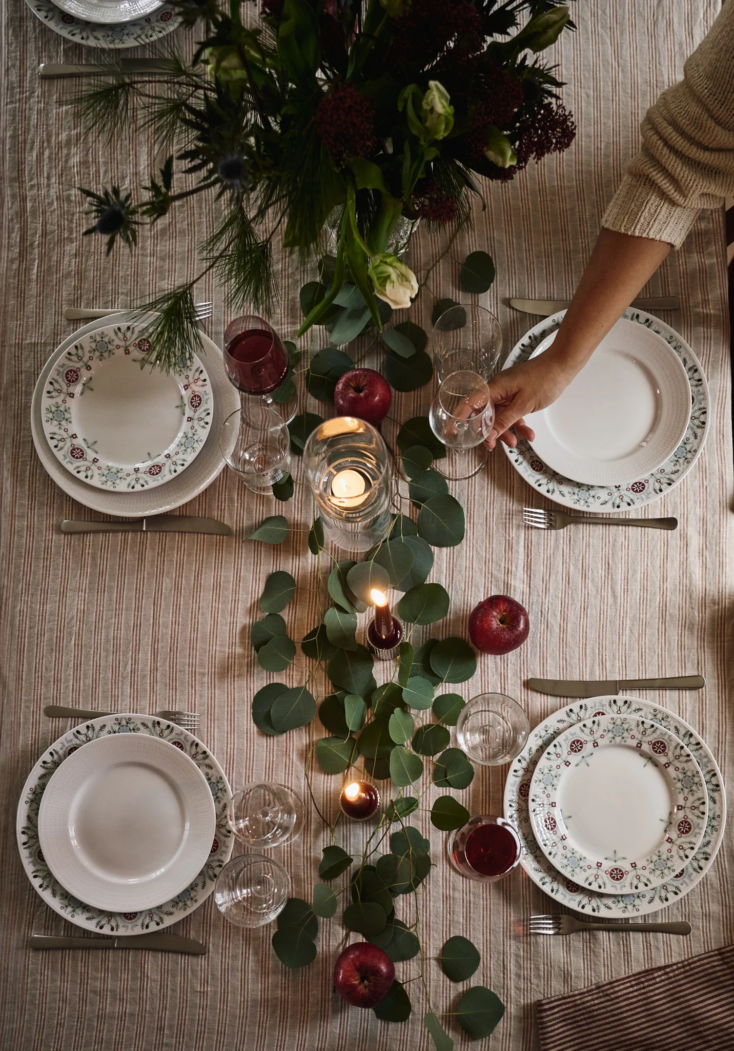 Une idée de table de Noël simple et élégante photographiée du dessus avec des feuilles vertes et des pommes rouges en guise de décoration. 