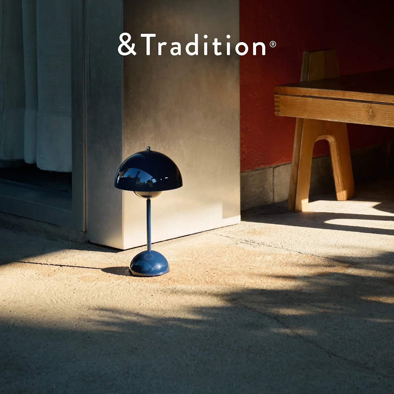 Une lampe de table bleu foncé en forme de champignon de &Tradition sur une terrasse ensoleillée, projetant des ombres distinctes.