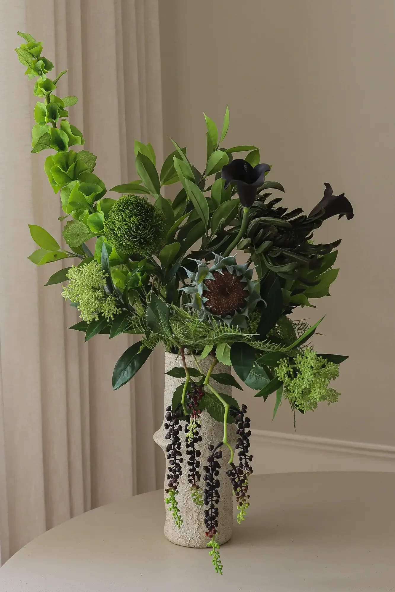 Un arrangement de feuillage vert, de lys calla foncés et de baies pendantes dans un vase texturé.