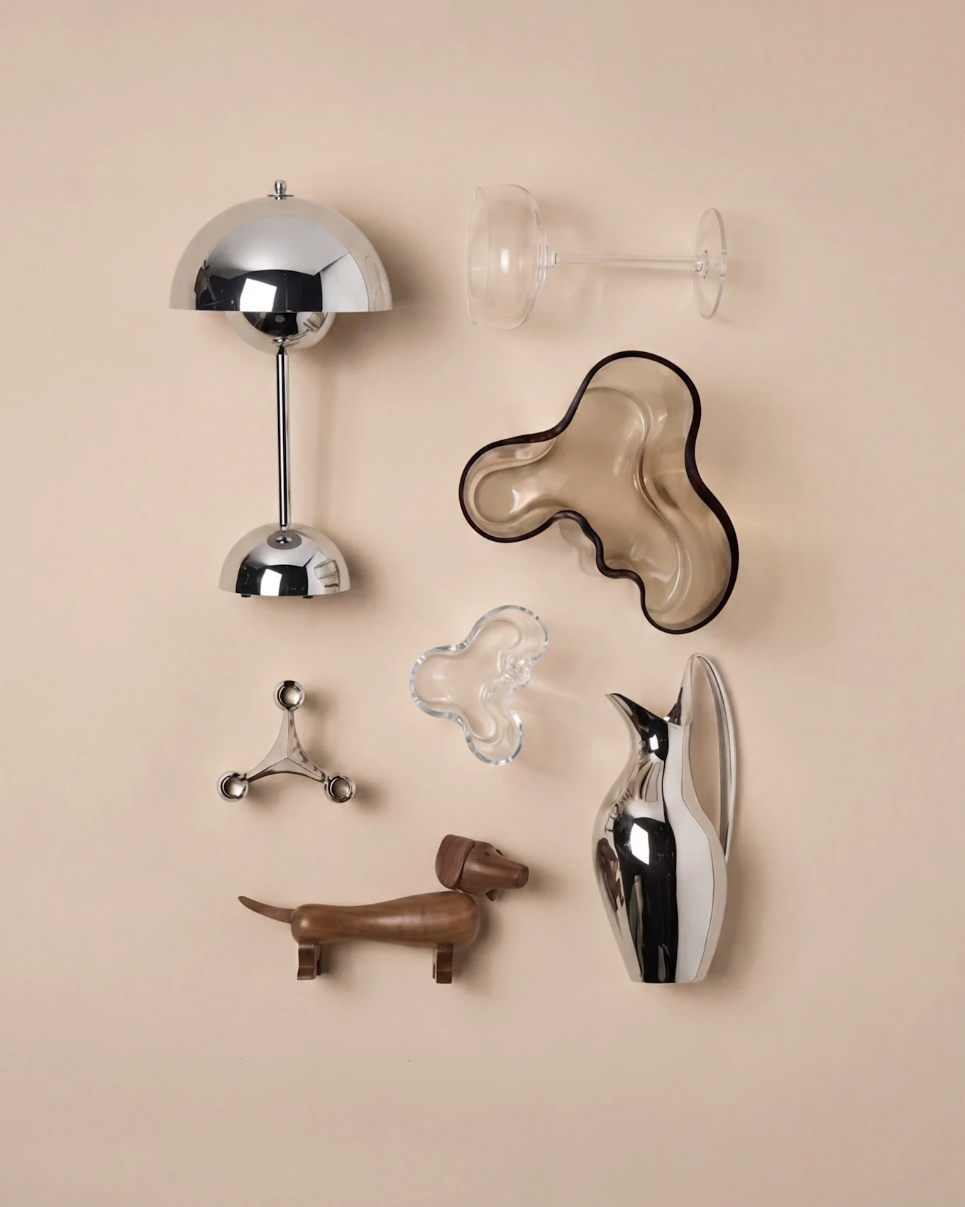 Décoration moderne: lampe champignon chrome, verre à vin, bol ondulé marron, bougeoir argenté, teckel en bois, carafe argentée.