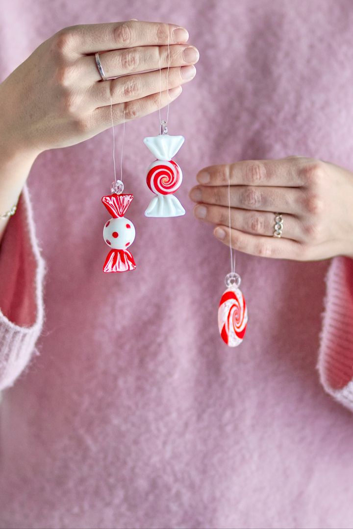 Décorations de Noël 2025 : une femme tient devant l'objectif trois pendentifs décoratifs festifs en forme de bonbons de la marque Bloomingville.