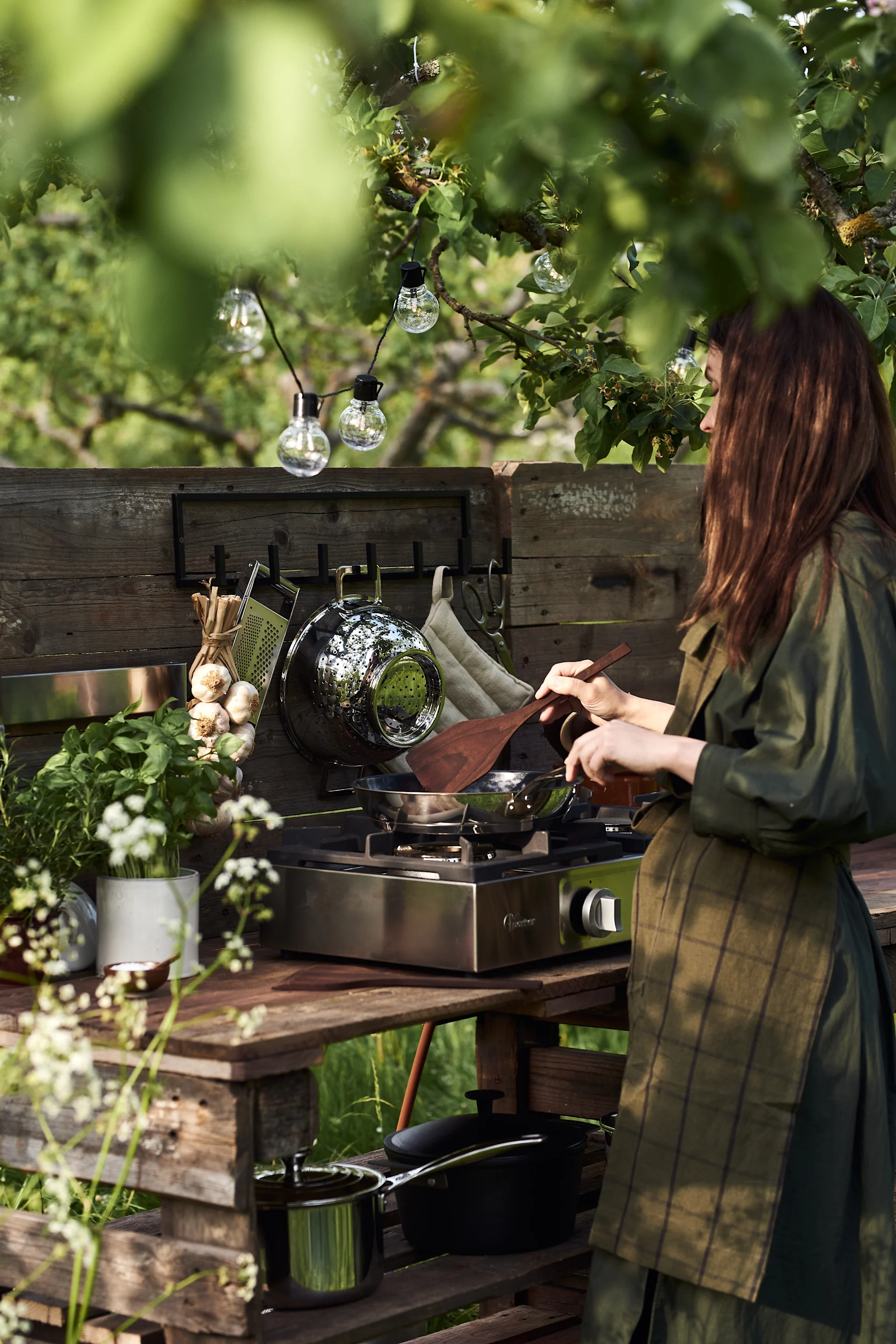 Une femme cuisine dans son jardin, dans sa petite cuisine d'extérieur qu'elle a elle-même construite à partir de palettes.