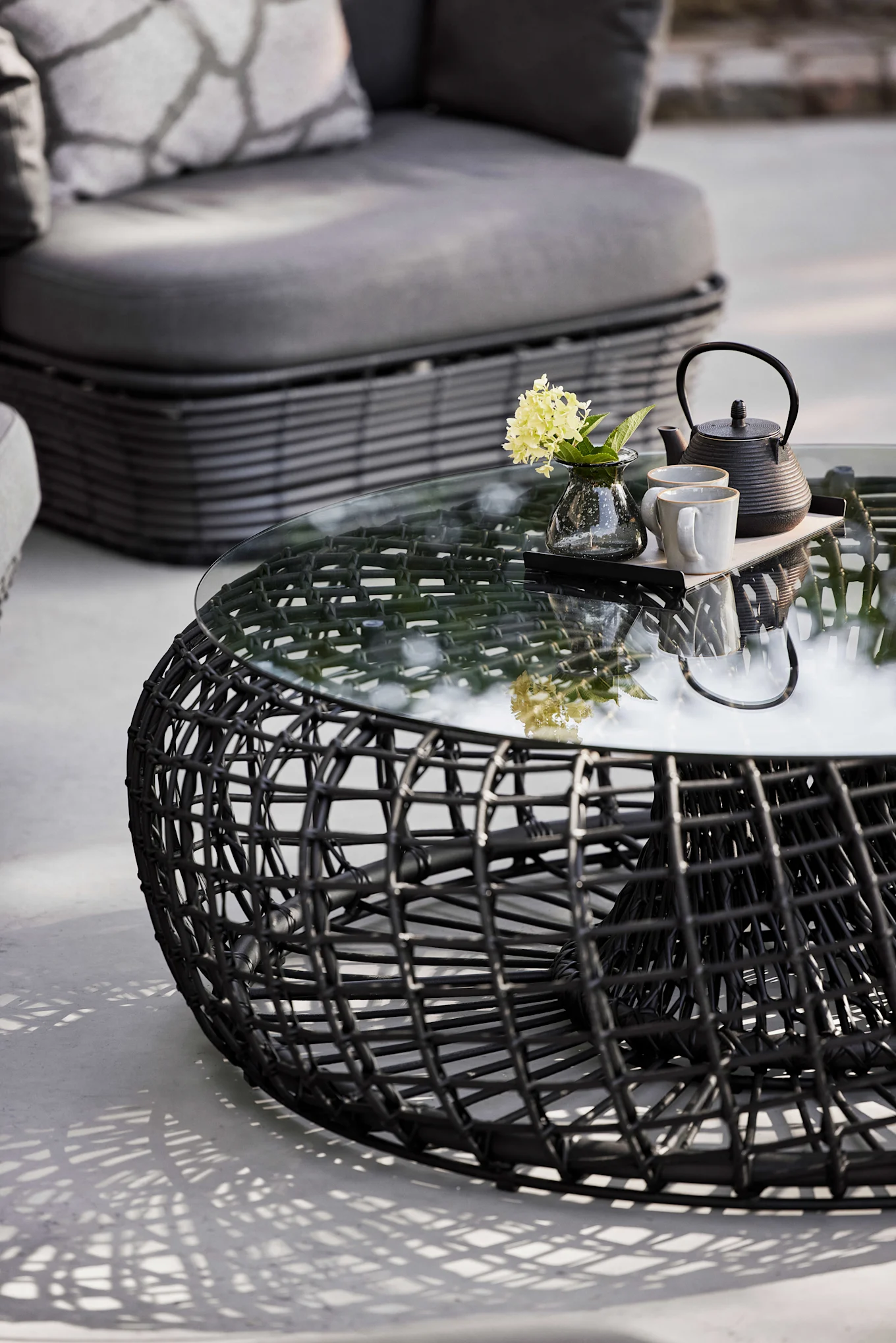 La table Nest de Cane-line en noir est composée de verre et d'aluminium et séduit par sa forme ronde - définitivement une tendance de meubles de jardin pour 2025.