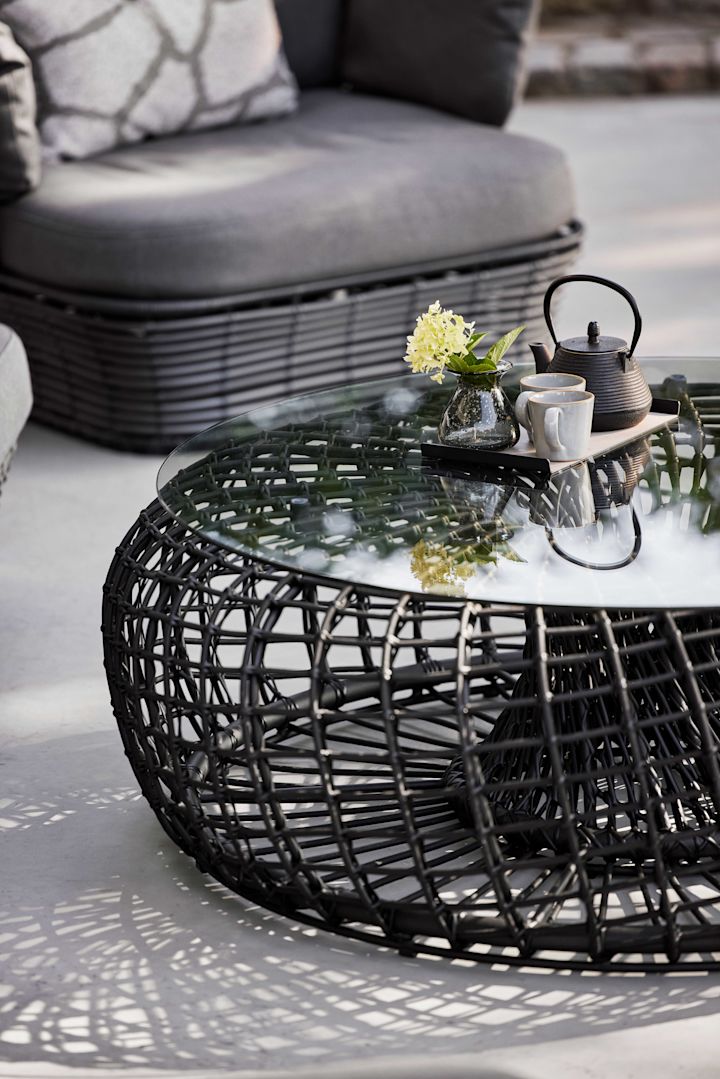 La table Nest de Cane-line en noir est composée de verre et d'aluminium et séduit par sa forme ronde - définitivement une tendance de meubles de jardin pour 2025.