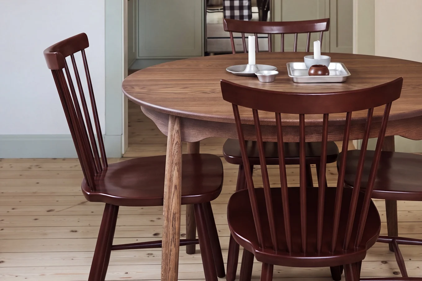 Salle à manger avec table ronde en bois, chaises rouges et suspension rouge, donnant sur une cuisine aux armoires vert clair.