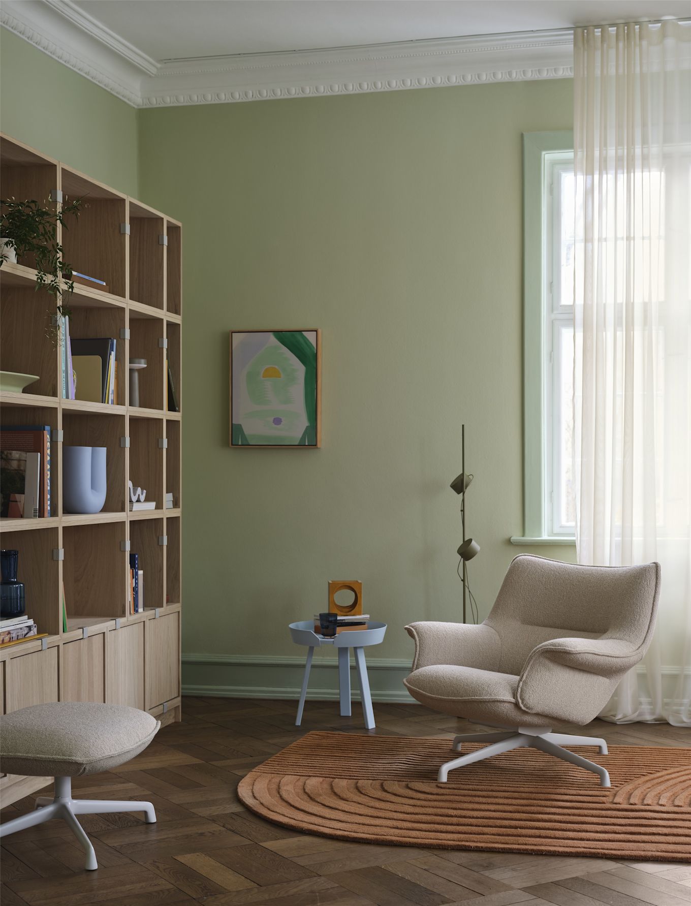 Le fauteuil Doze de Muuto, de couleur beige, se trouve devant une étagère dans un salon meublé de manière confortable.