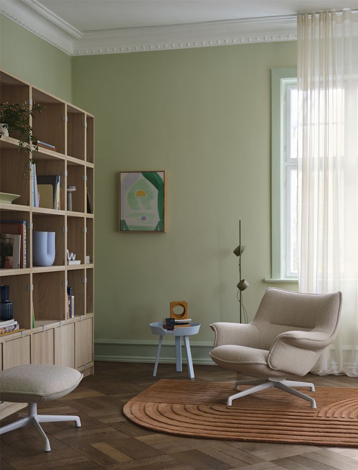 Le fauteuil Doze de Muuto, de couleur beige, se trouve devant une étagère dans un salon meublé de manière confortable.