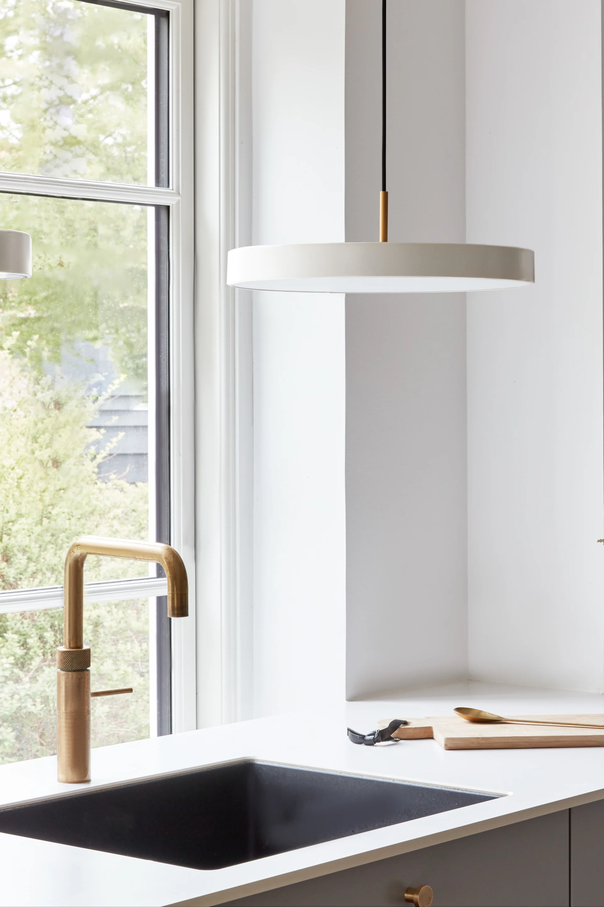 Utilisez de grandes lampes suspendues si vous avez besoin d'un peu plus de lumière dans des endroits comme l'évier. Ici, vous pouvez voir la suspension Asteria Micro en blanc perle de Umage suspendue au-dessus d'un évier.