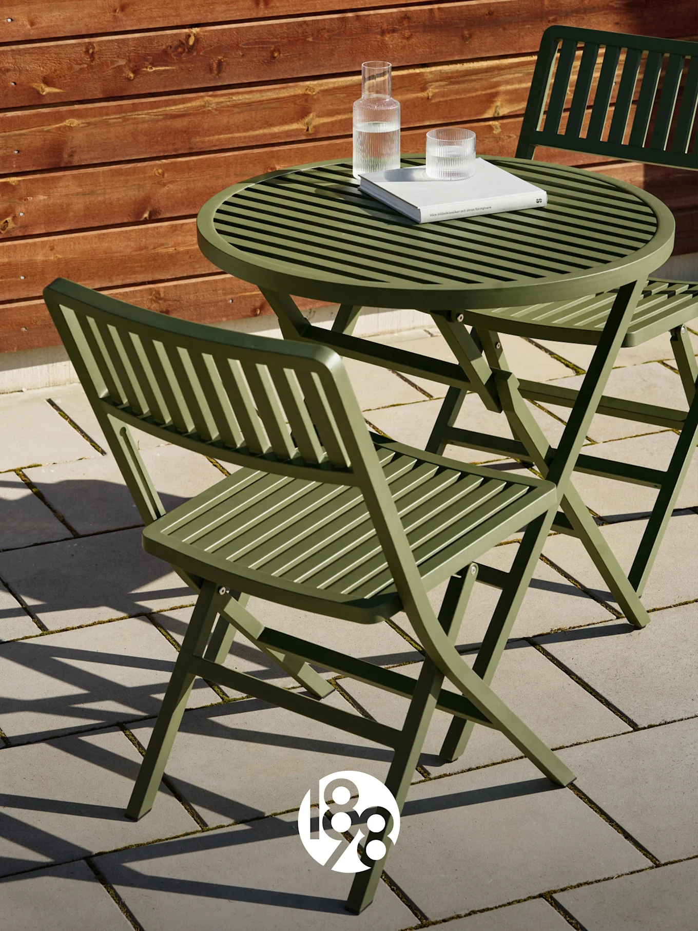 Deux chaises pliantes vertes à lattes et une table assortie sur un patio avec un livre et des verres d'eau.