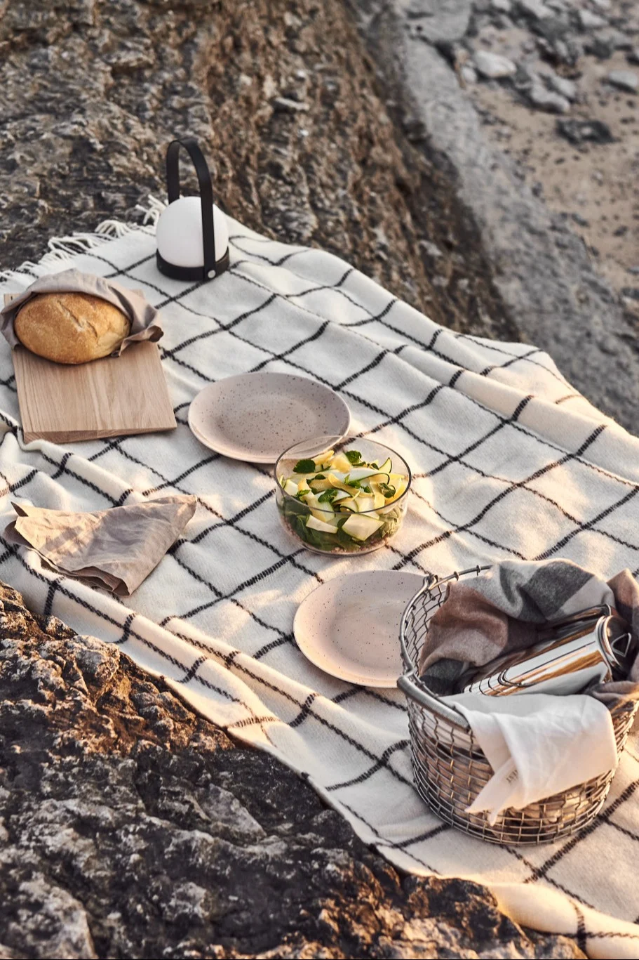 Pique-nique sur des rochers avec une nappe à carreaux, du pain, une lanterne, de la salade, des assiettes et un panier.