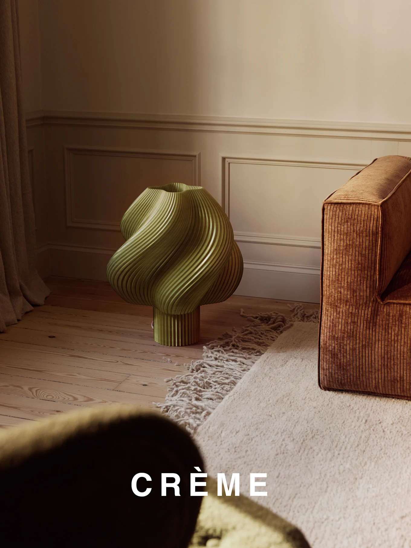 Une lampe vert clair, torsadée et côtelée, sur un parquet en bois, à côté d'un canapé côtelé marron et d'un tapis shaggy beige.