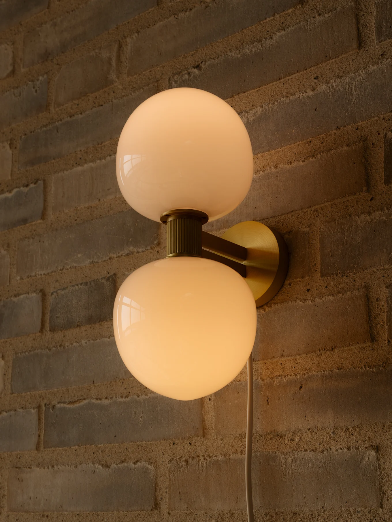 Applique murale avec deux globes en verre sphériques blanc laiteux et une monture en laiton sur un mur de briques.