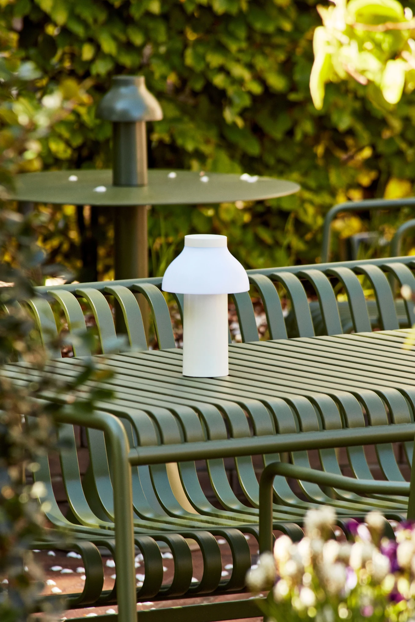 La lampe de table PC potable blanche est une lampe rechargeable qui se place à l'extérieur sur une table verte. 