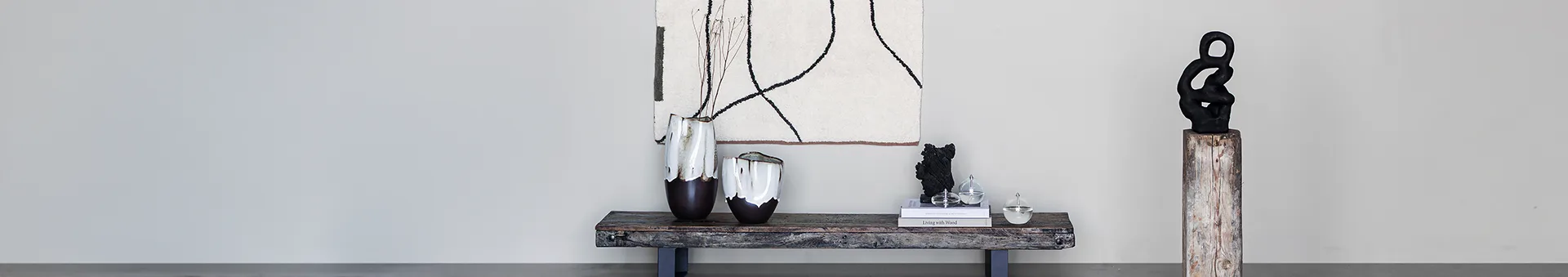 Intérieur moderne avec art abstrait, deux vases marron et blancs sur un banc rustique, et une sculpture noire sur un piédestal.