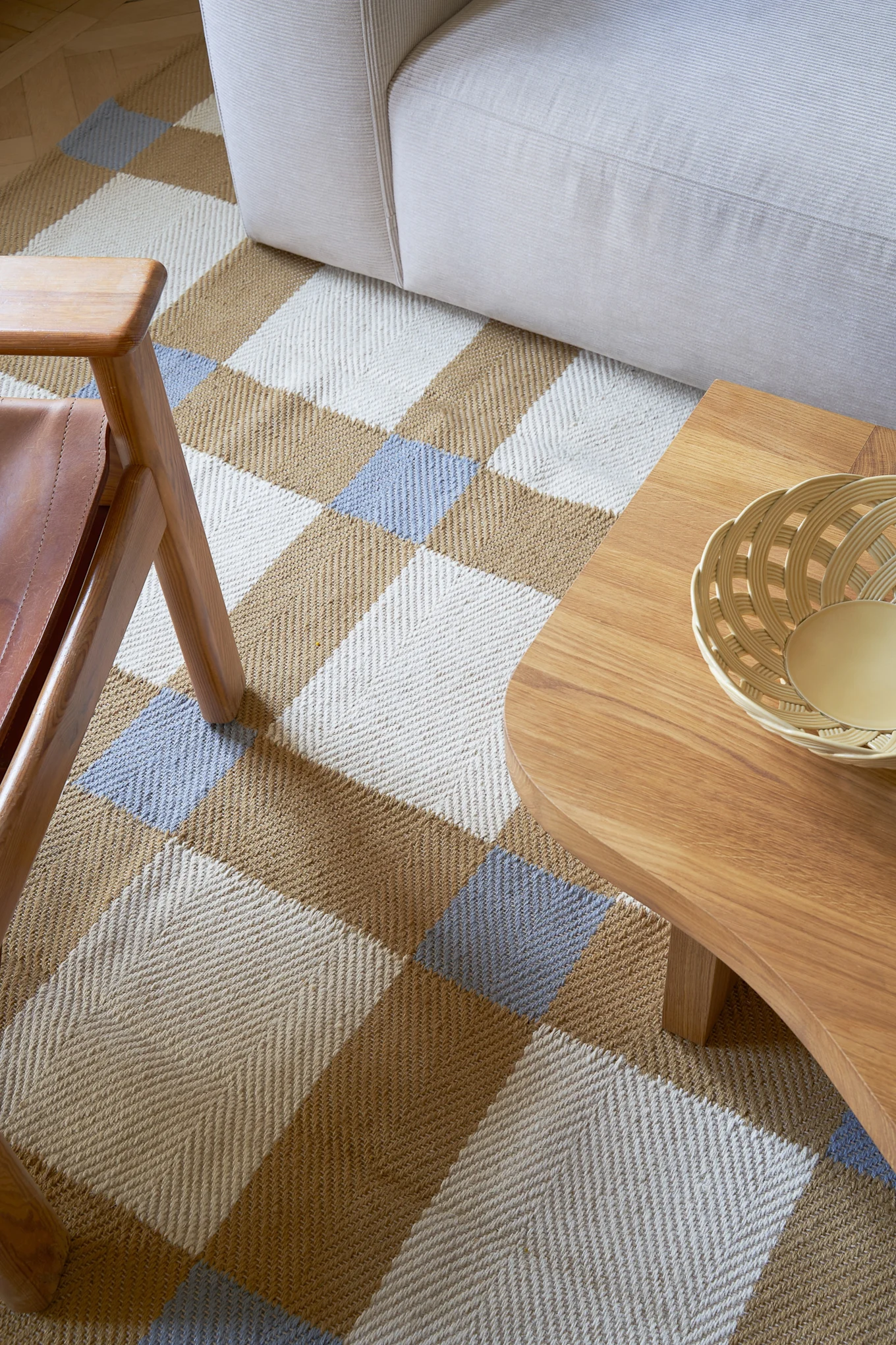 Vue d'ensemble d'un salon avec un tapis à motif en chevrons blanc, marron et bleu clair, un canapé couleur crème et une table basse en bois.