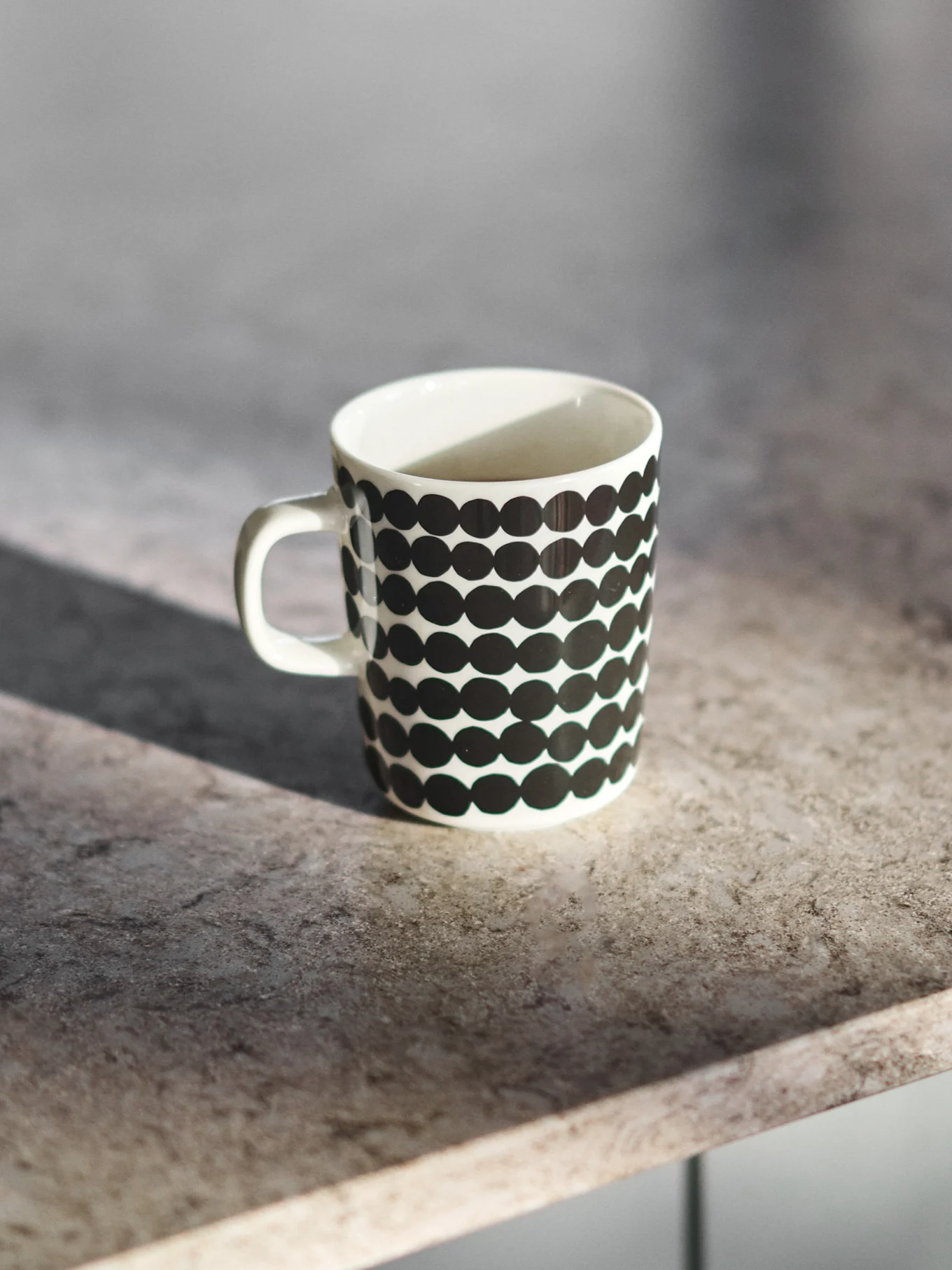 Mug en céramique blanc à pois noirs sur un comptoir gris.
