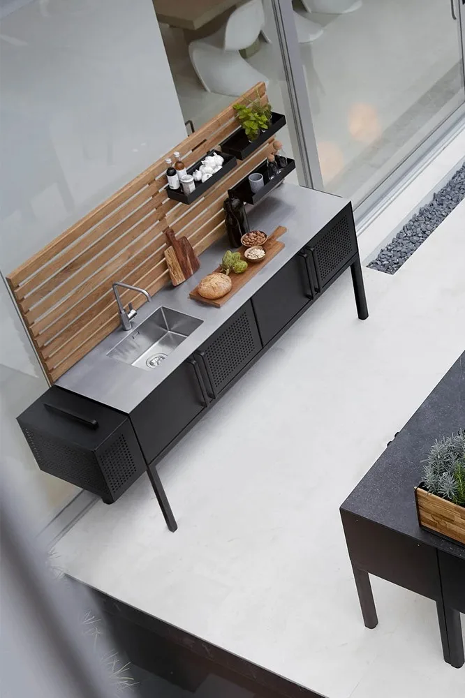Cuisine d'extérieur moderne avec évier en acier inoxydable, armoires noires, panneau arrière en bois et étagères pour les épices et les provisions.