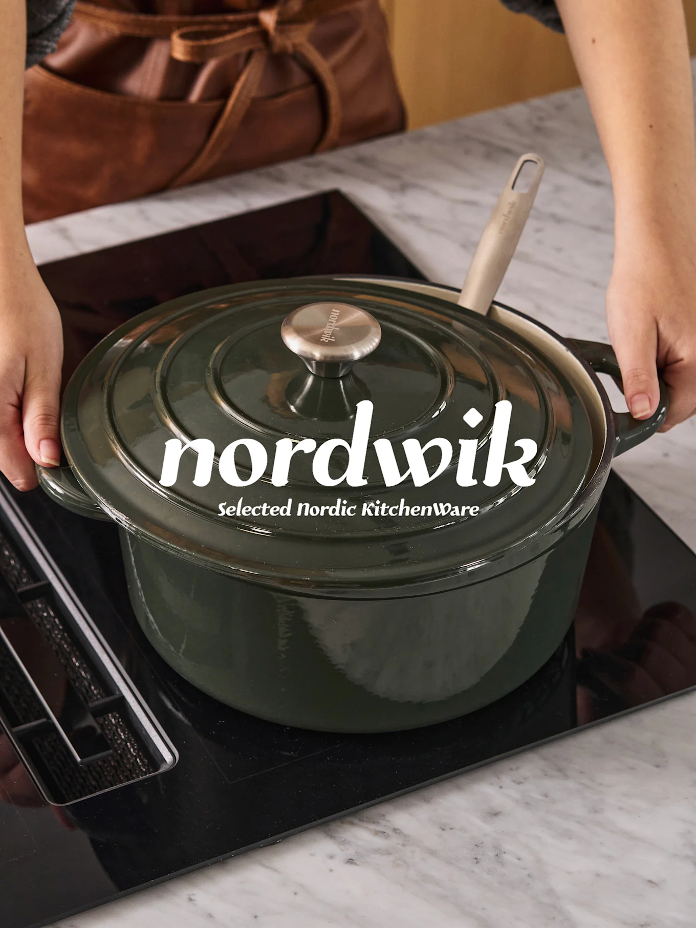 Mains plaçant une cocotte vert foncé avec une cuillère claire sur une plaque à induction noire. Le logo 'nordwik' est visible sur le couvercle.