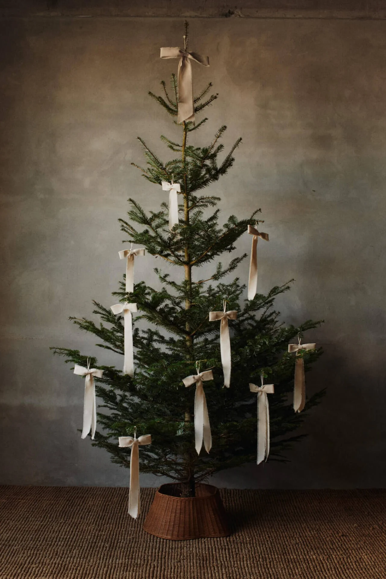 Quatre bougies blanches allumées, disposées sur un plateau en bois avec une pomme de pin et des branches de sapin, sur une table en bois.