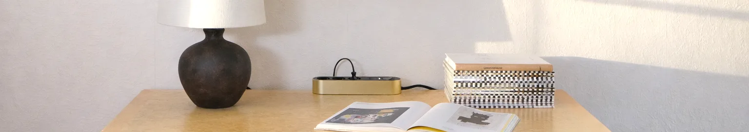 Multiprise dorée avec trois prises noires et un bouton d'alimentation sur une surface claire.