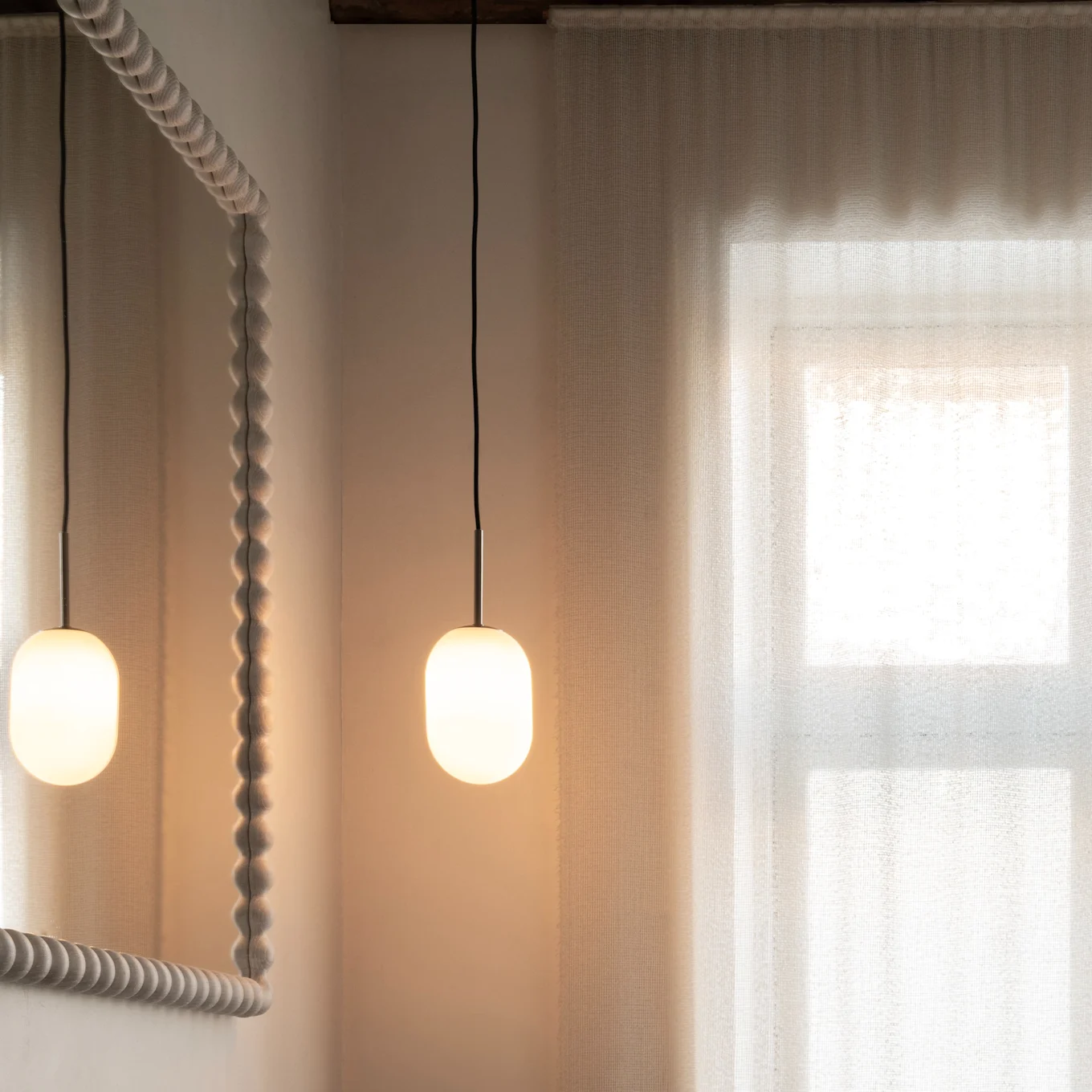 Salle de bain moderne: meuble vasque en bois, lavabo foncé, robinet bronze, miroir texturé, suspensions, rideaux transparents.