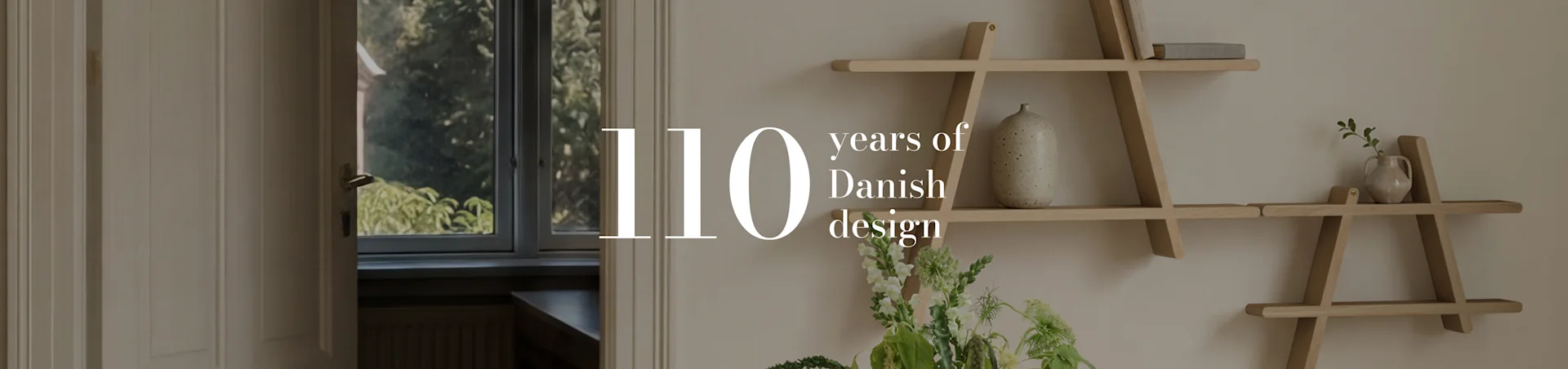 Texte '110 years of Danish design' sur une photo d'intérieur d'une pièce avec une étagère géométrique en bois, un vase et des fleurs.