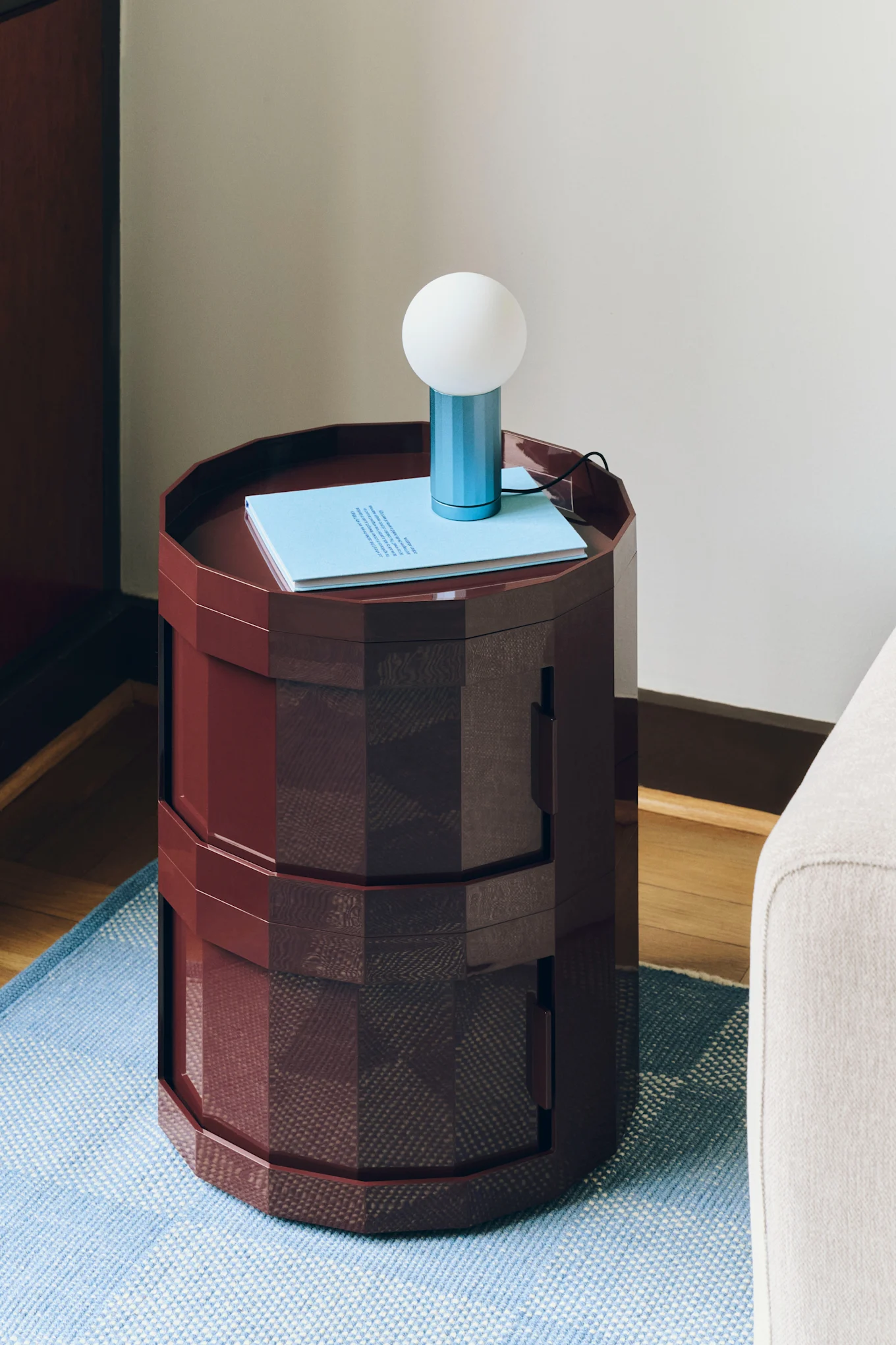 Table d'appoint hexagonale rouge foncé, sur laquelle sont posés un livre bleu clair et une petite lampe bleue et blanche, posée sur un tapis à motifs bleus.