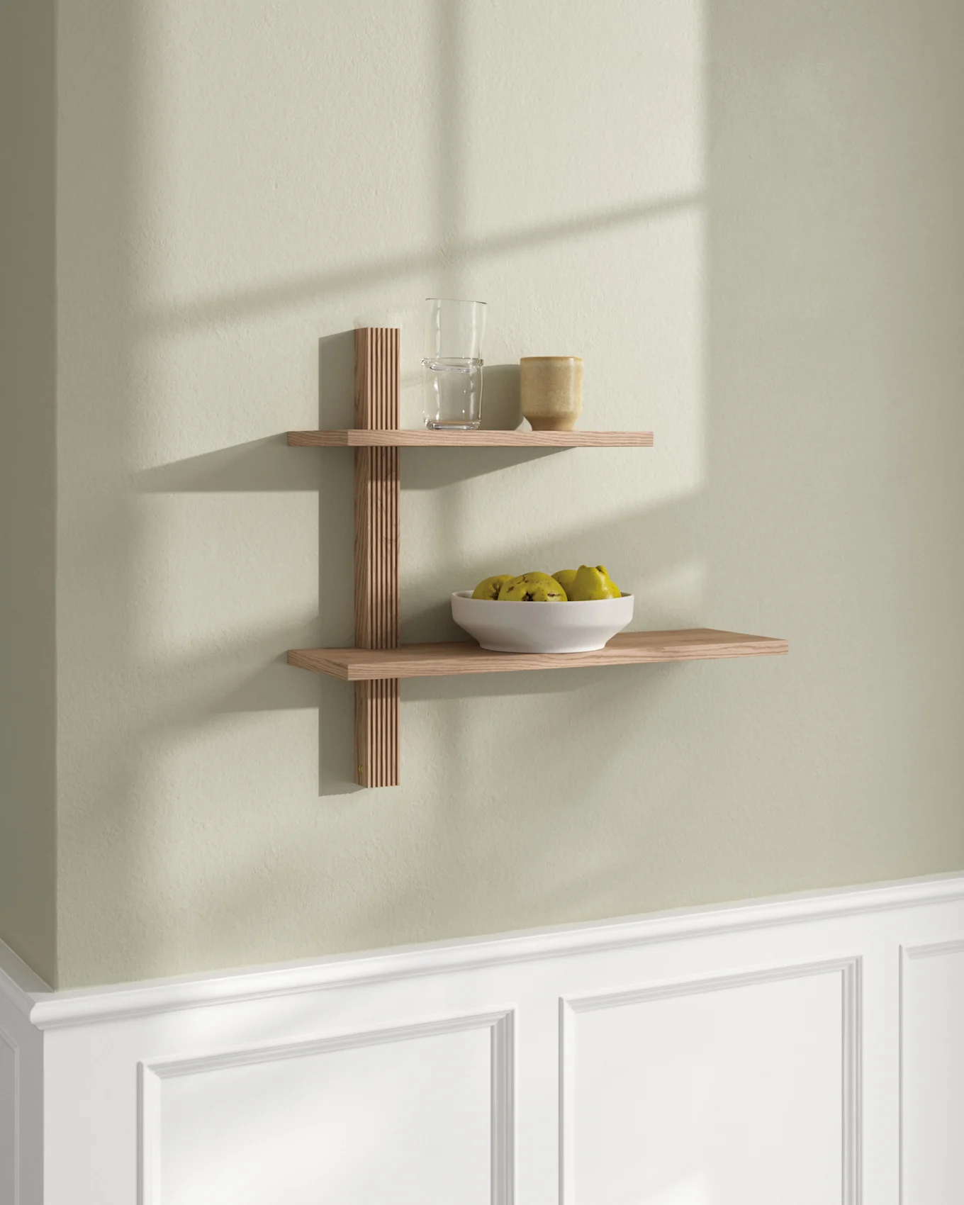Deux étagères flottantes en bois clair sur un mur vert pâle. L'étagère supérieure a un verre et une tasse; l'inférieure, un bol de fruits.
