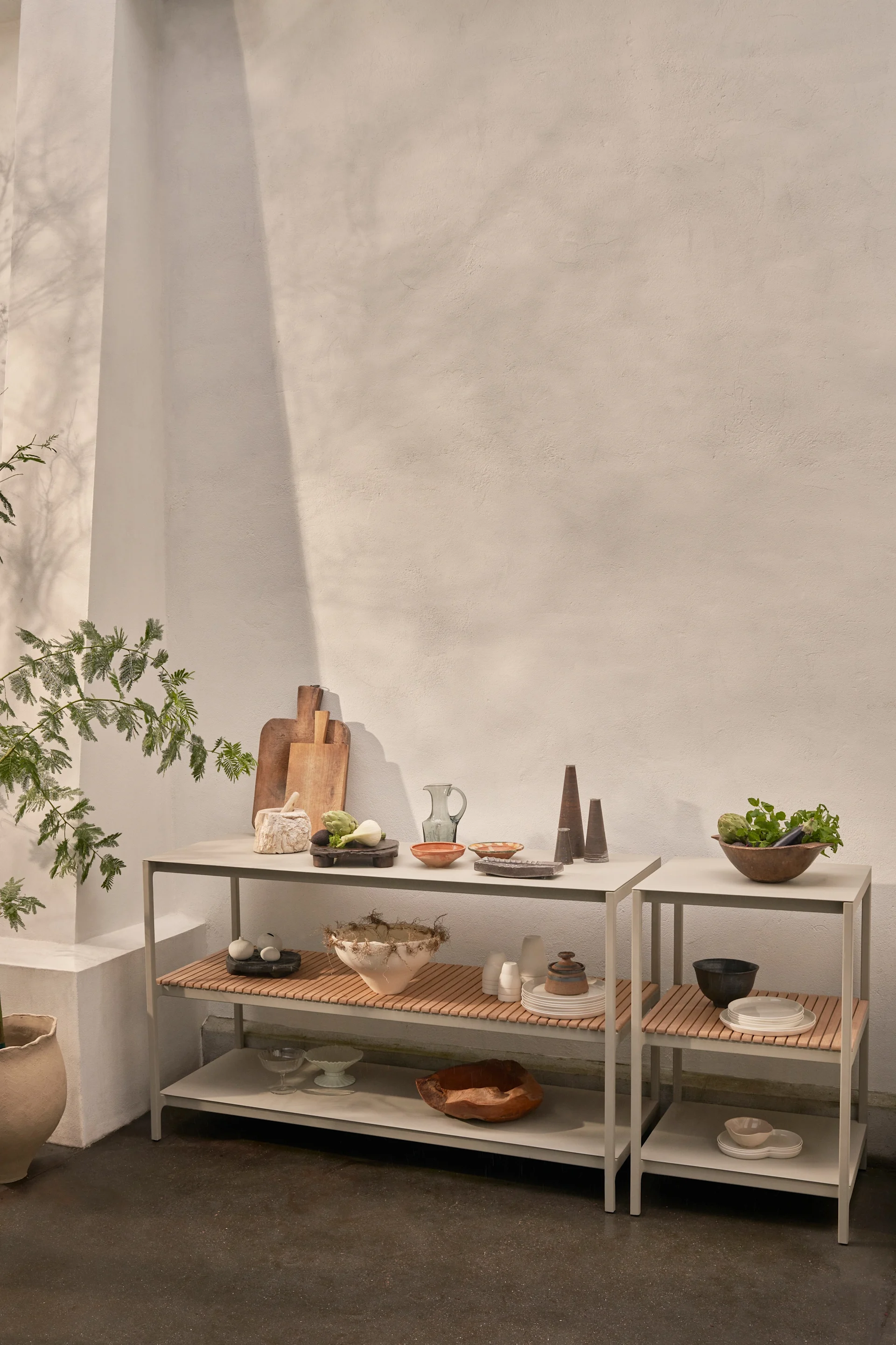 Deux étagères modernes grises ornées de lattes en bois présentent divers ustensiles de cuisine, des bols en céramique, des légumes frais et des objets décoratifs devant un mur clair.