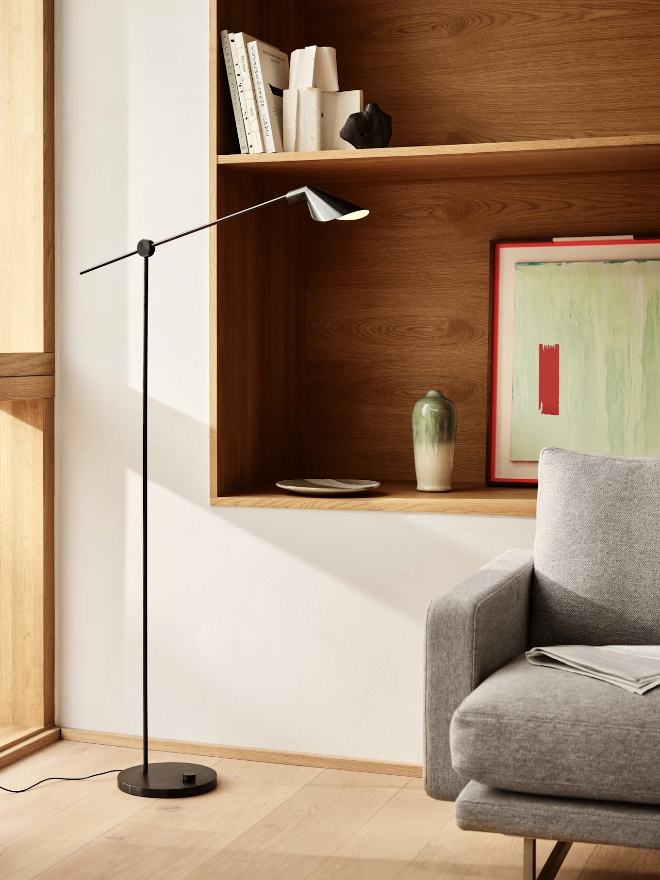 Un salon moderne avec un lampadaire noir épuré, des étagères en bois avec des livres et de la décoration, et une partie d'un canapé gris.