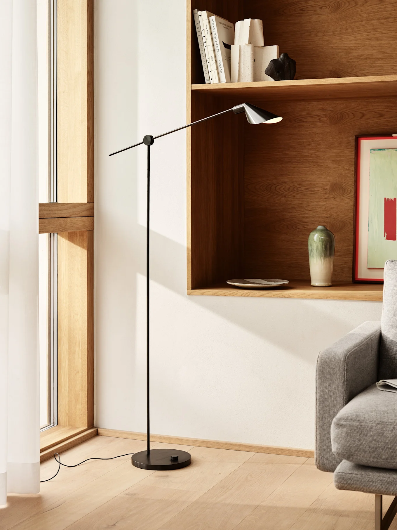 Lampadaire noir haut et élancé avec bras réglable et abat-jour foncé dans un salon moderne avec étagères en bois.
