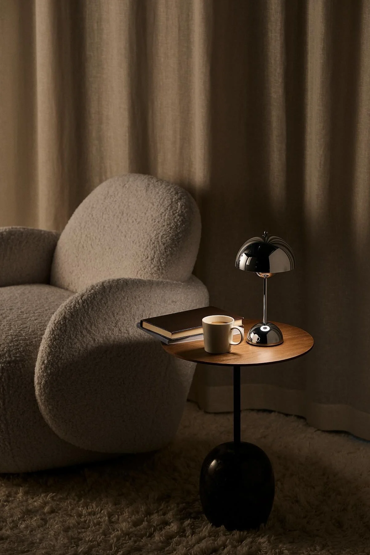 À côté du fauteuil Mo de 1898 se trouve une table basse avec un livre, une tasse de café et la lampe de table Flowerpot chromée de &Tradition.