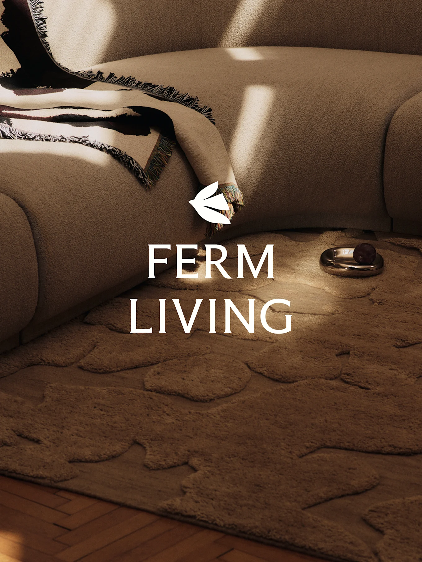 Une scène cosy avec un canapé texturé marron clair, une couverture à motifs, un tapis marron aux formes organiques et un plat décoratif.