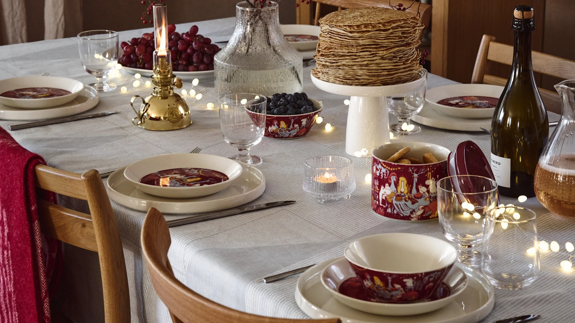 Sur une table dressée pour les fêtes, on trouve une pile de crêpes ainsi que divers articles de la collection Festive Moments de Moomin Arabia.