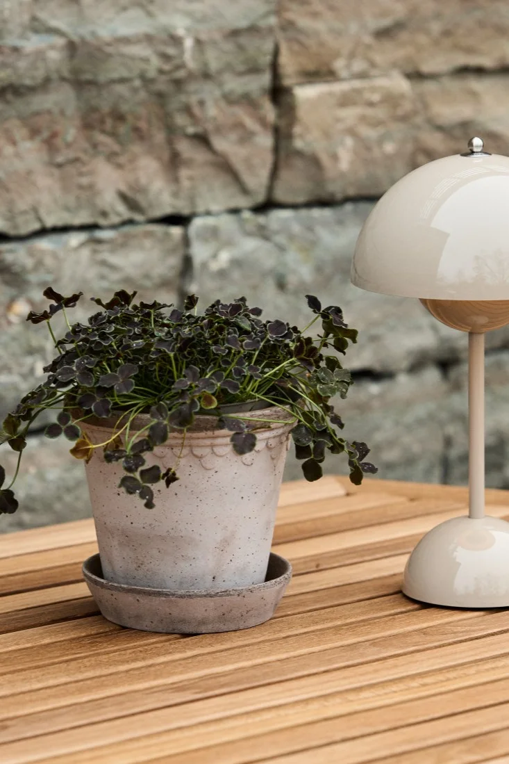 Le pot de fleurs d'extérieur Copenhangen est posé sur une table à manger en bois avec la lampe de table portable Flowerpot Vp9. 
