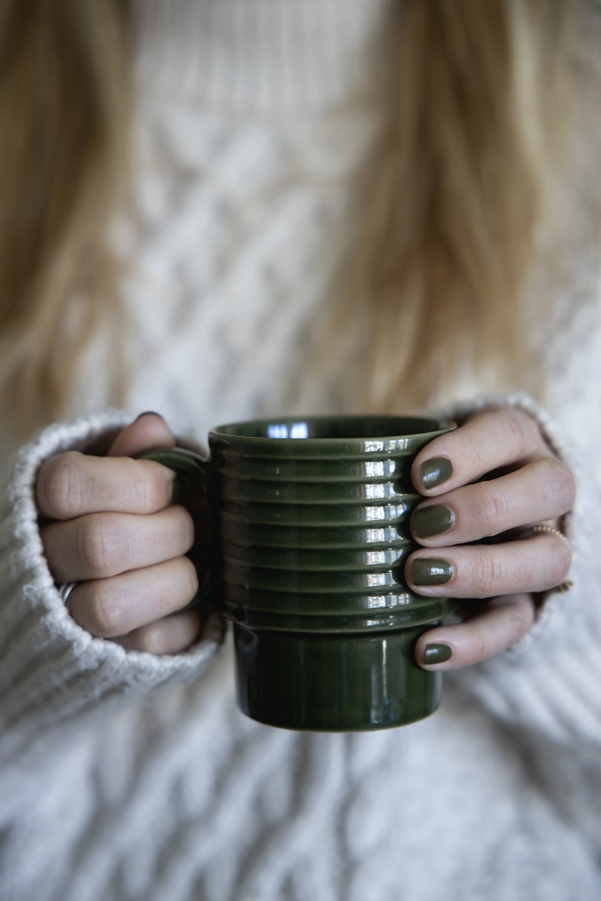Une femme vêtue d'un pull blanc tient dans ses mains une tasse verte de la collection Coffee & More de Sagaform.