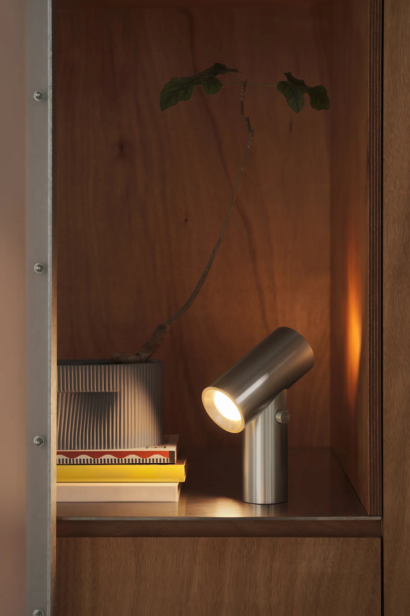 La lampe rechargeable Beam de Muuto est posée sur une étagère à côté de livres et éclaire la pièce. 