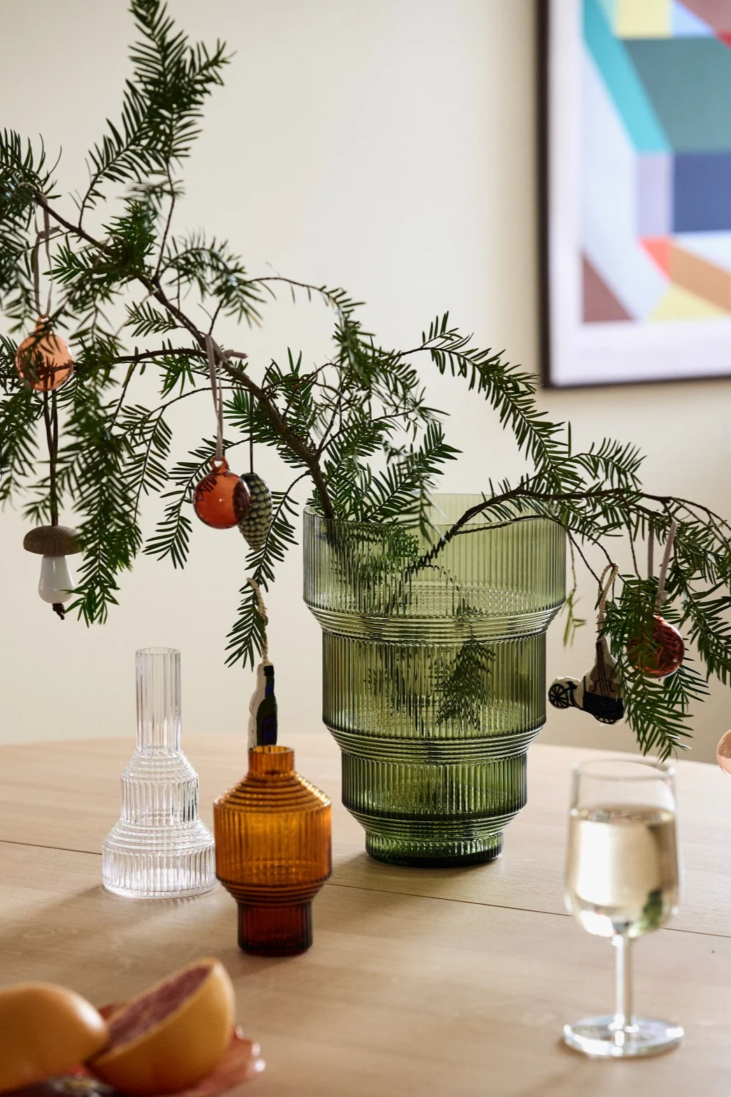Fabriquer des décorations de Noël avec du sapin : ici, vous pouvez voir des branches de sapin dans le vase Pavillon vert de Kosta Boda, décorées de boules de Noël, posées sur une table.