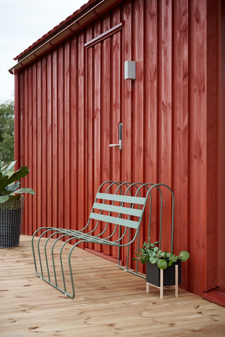 Tendances 2025 en matière de meubles de jardin : le Gardeners Sofa de Design House Stockholm en vert est placé sur une terrasse devant une maison en bois rouge suédoise.
