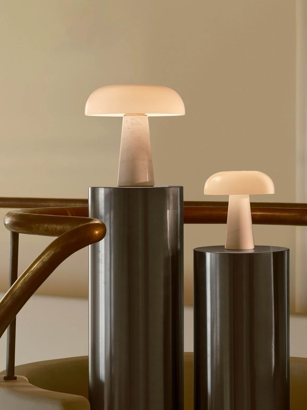 Deux lampes de table lumineuses en forme de champignon, une grande et une petite, sur des socles cylindriques près d'une rampe en laiton.