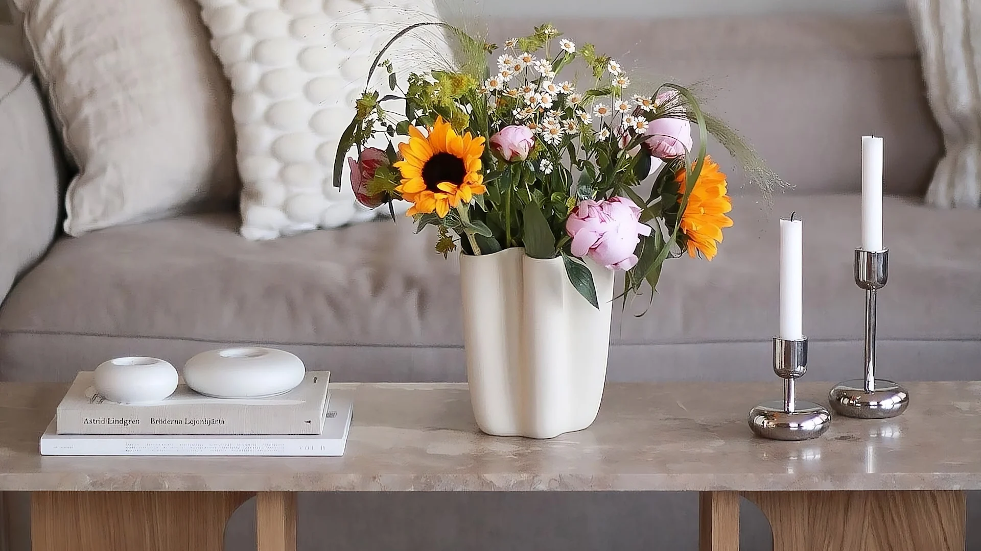 La table basse androgyne d'Audo Copenhagen est décorée de fleurs fraîches, de deux bougeoirs Nappula d'Iittala et des photophores Stone de Scandi Living.