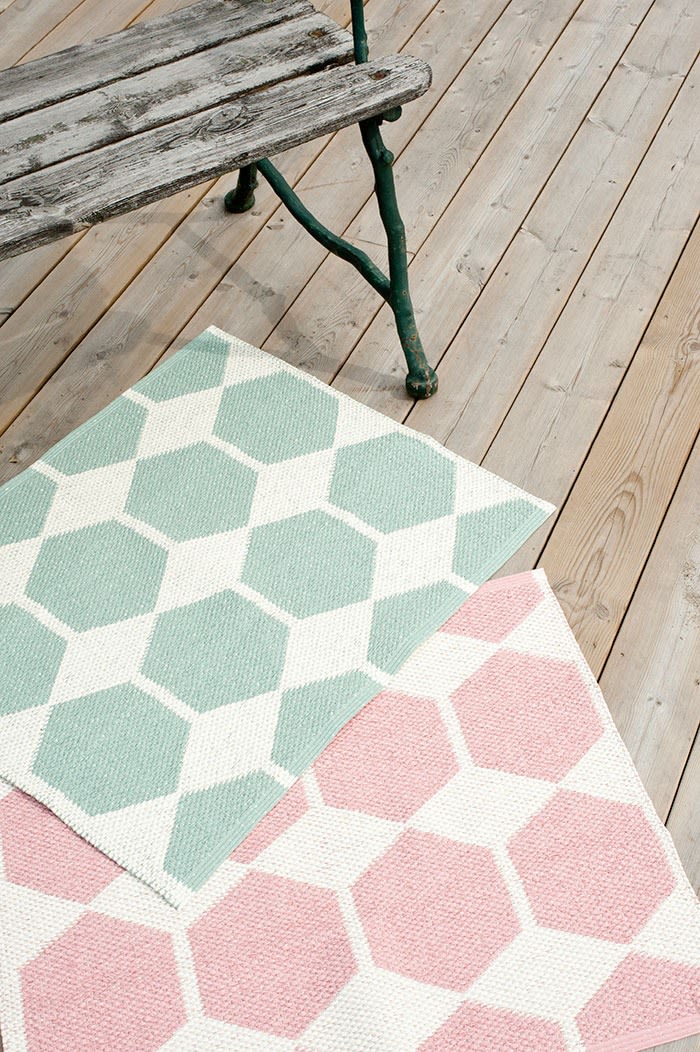 Tapis d'extérieur : vous voyez ici le tapis d'extérieur vert et le tapis d'extérieur rose de Brita Sweden posés devant un banc sur une terrasse en bois.
