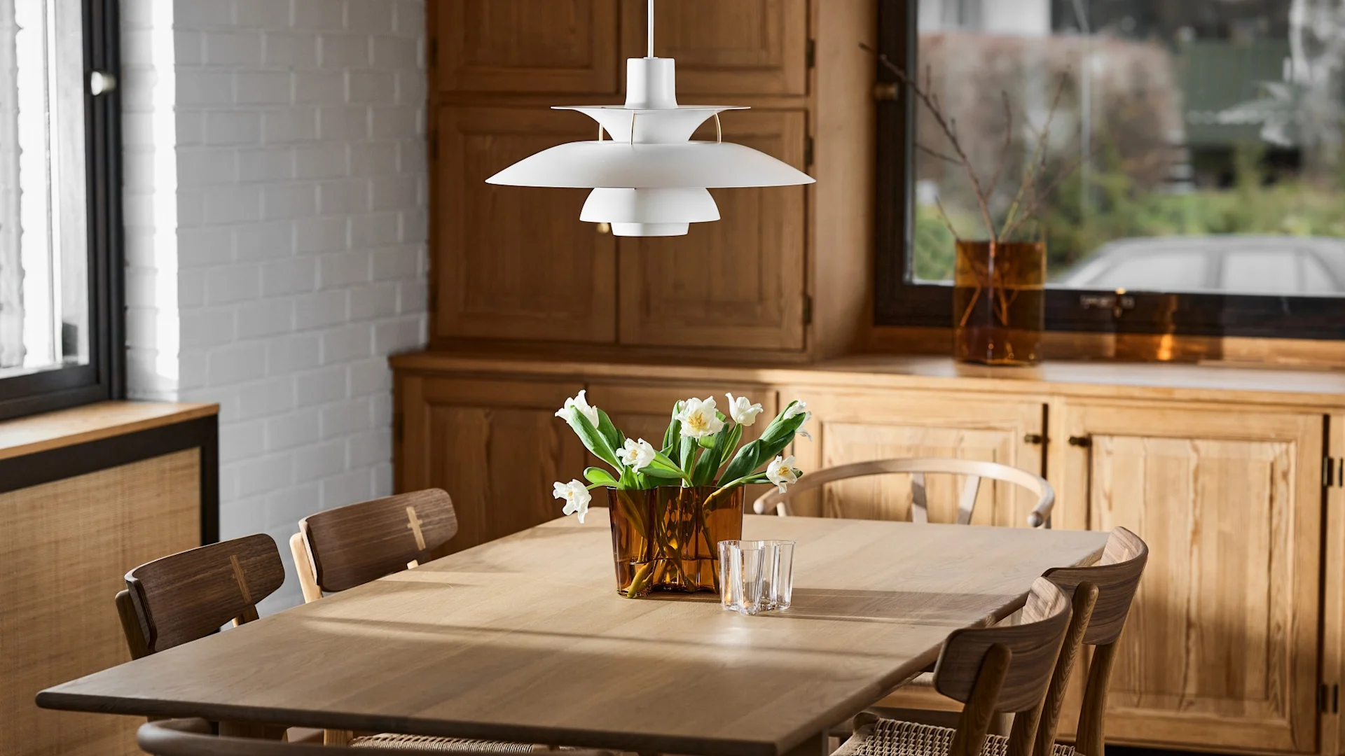 Sur une table à manger dans une cuisine scandinave se trouve le vase Aalto avec des jonquilles.