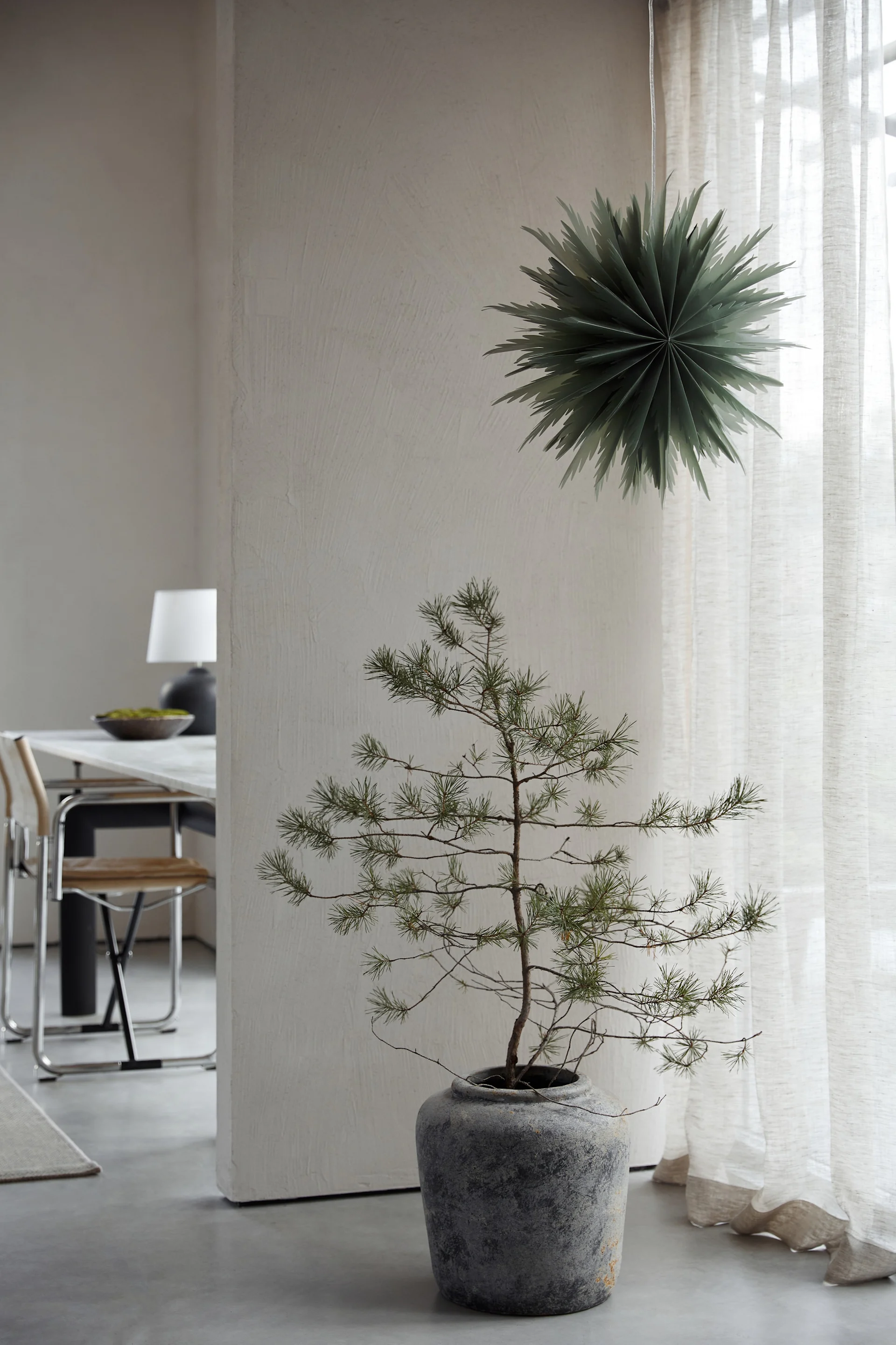 Sapin de Noël avec bougies, clochettes et flocons de neige à côté d'une armoire avec un vase décoratif.