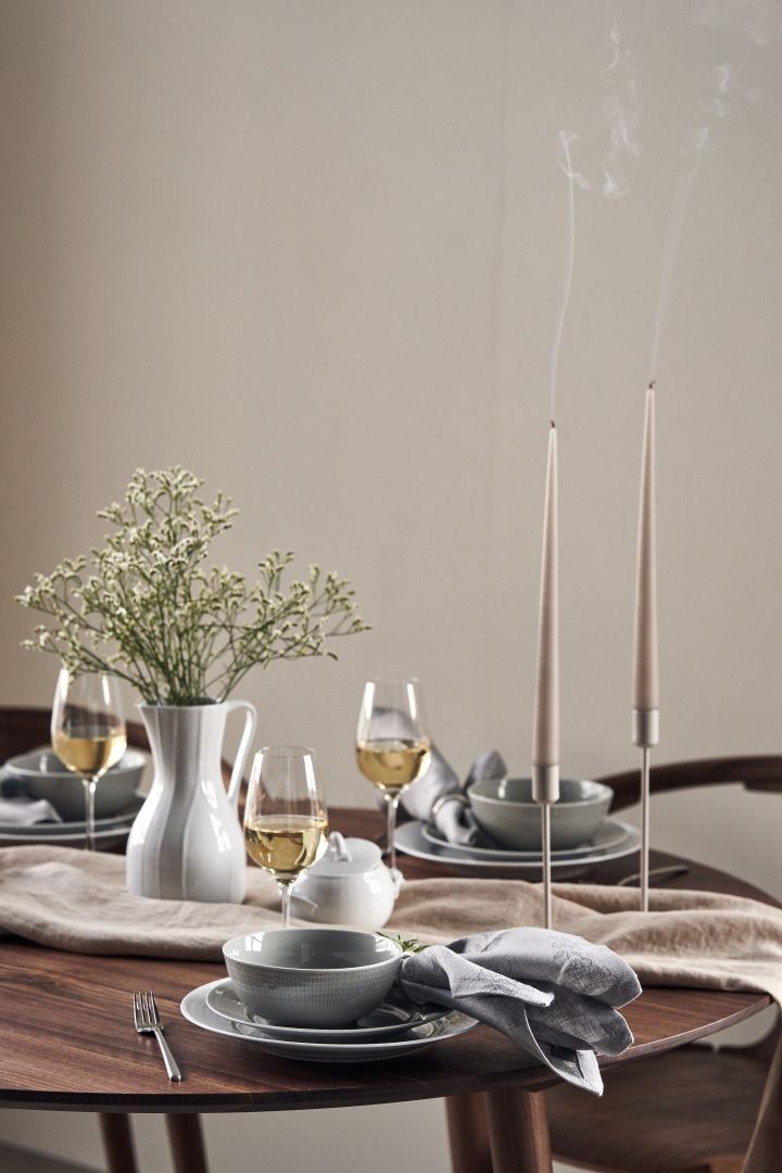 Une table festive avec des bougies, des fleurs de prairie dans une carafe de Pli Blanc et de la porcelaine Swedish Grace en blanc et gris.