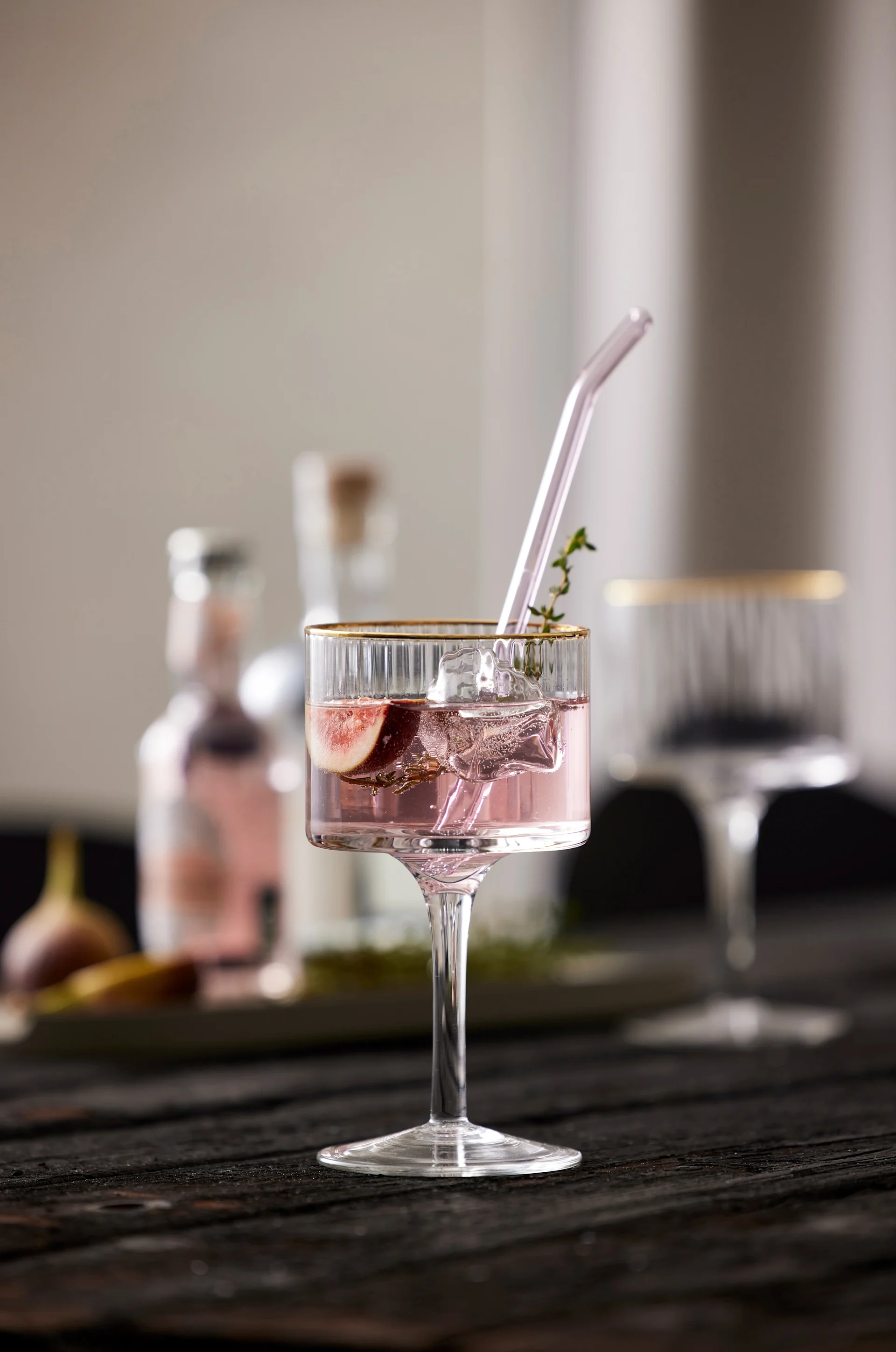 Un mocktail violet avec une paille en verre et décoré de thym est posé sur une table, servi dans un verre Palermo Gold Gin & Tonic de Lyngby Glas.