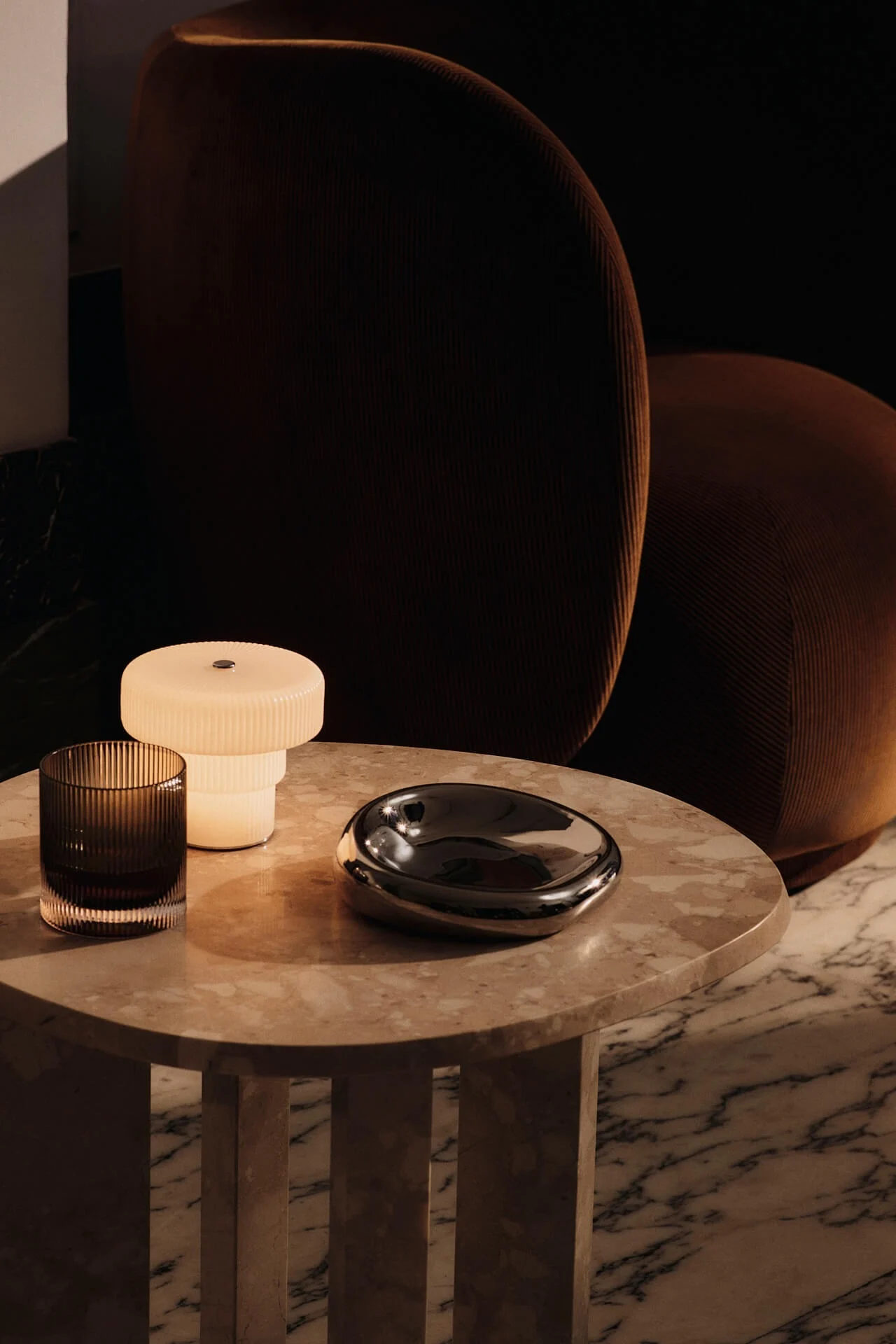 La lampe portable Ripple est posée sur une table d'appoint en pierre, à côté d'un fauteuil Rico.