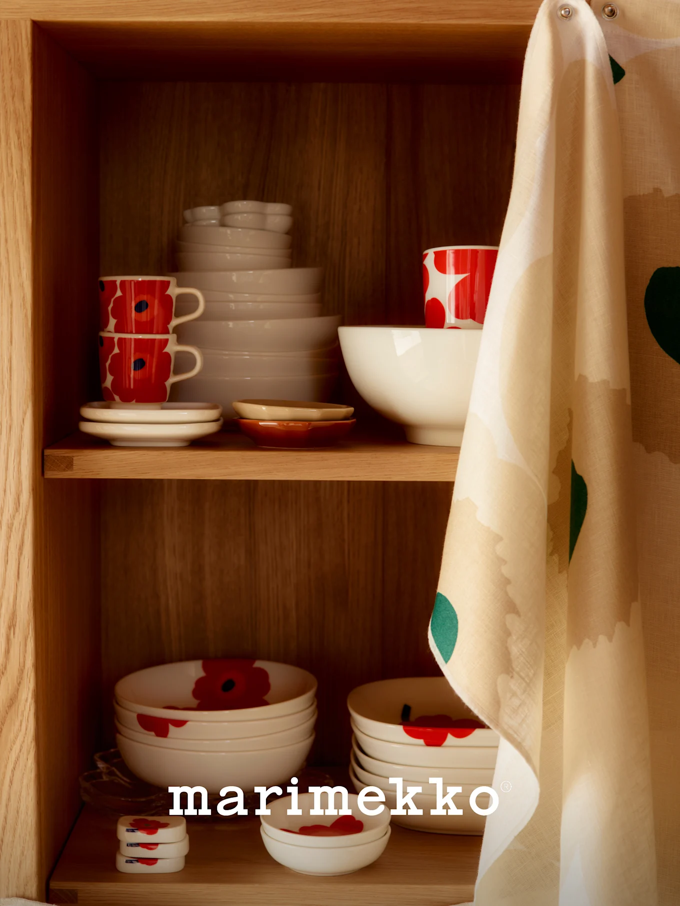 Une étagère en bois avec de la vaisselle en céramique blanche, certaines avec un motif de coquelicots rouges, et un torchon à motifs accroché sur le côté.