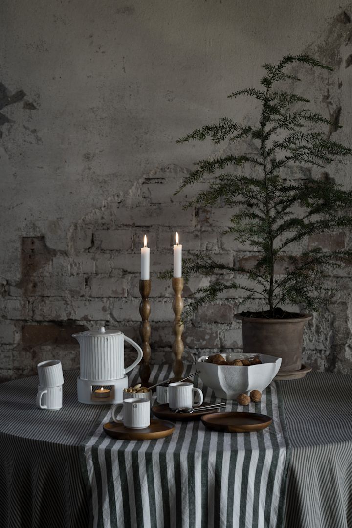 Une table dressée avec de la vaisselle, un pichet, des bougeoirs et la nappe rayée verte et blanche d'Ernst.